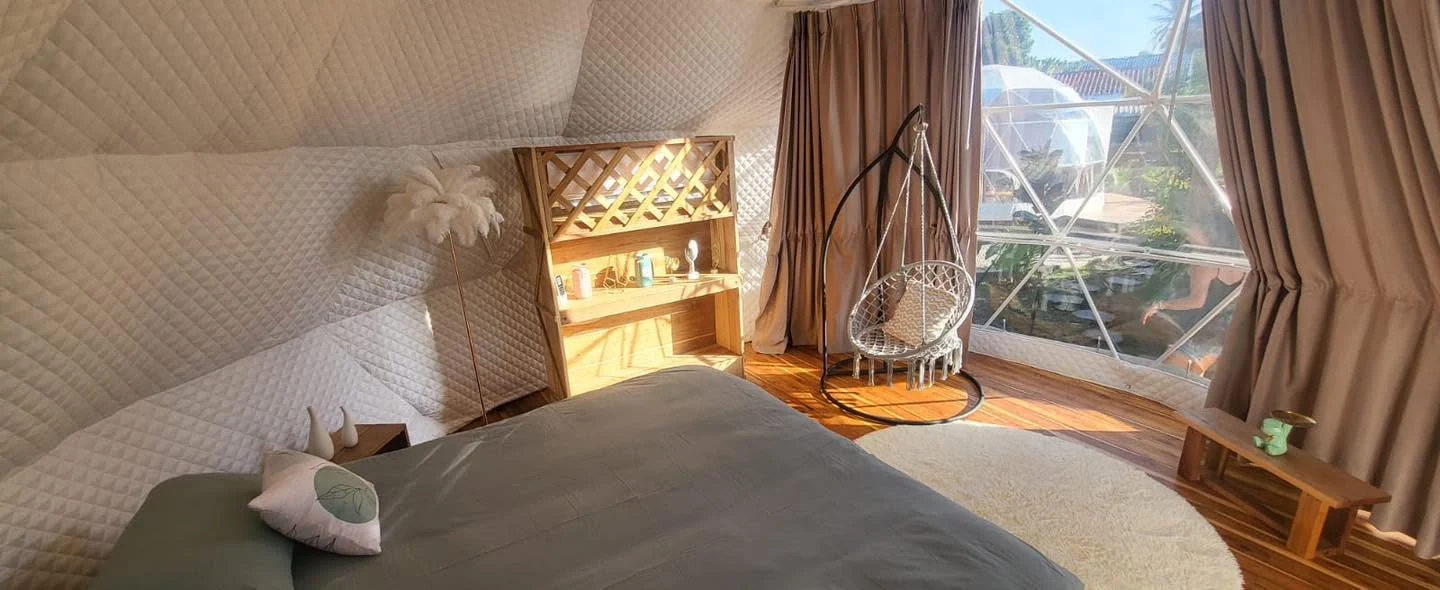 A comfortable bed and hanging chair inside a Domea dome